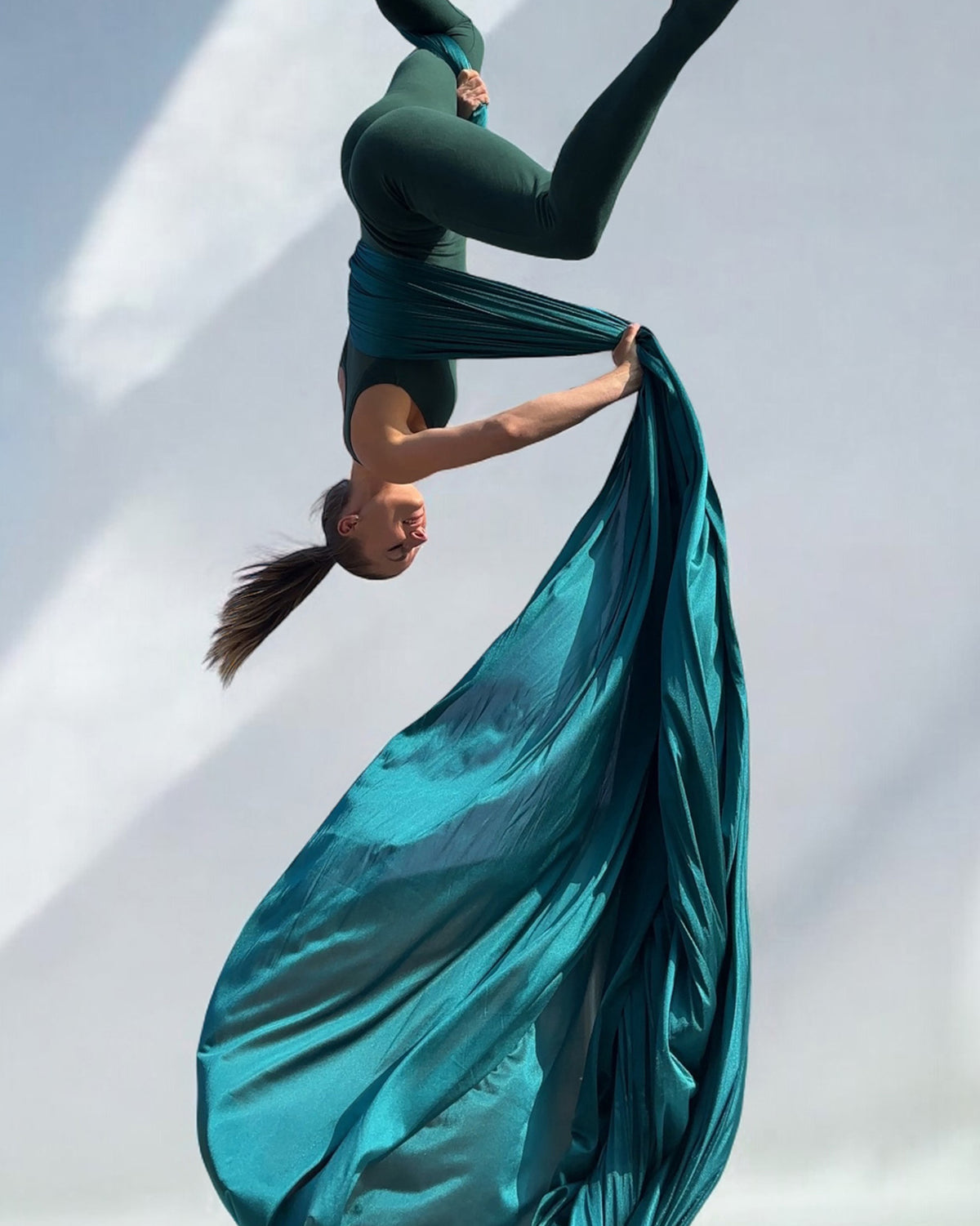 Person performing aerial silks acrobatics with Jade green fabric against a light background